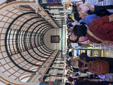 Crowds of visitors inside Saigon Central Post Office below its vaulted glass-paneled ceiling and large clock.