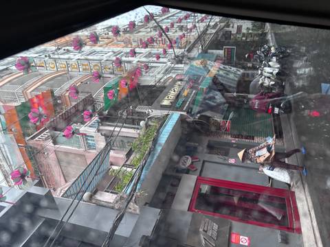 Rain-streaked bus window view of a narrow Vietnamese street with colourful lanterns and shop signs.