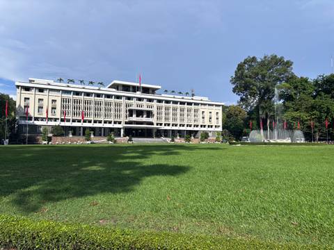 The Independence Palace stands behind manicured lawns and fluttering flags under bright sunshine.