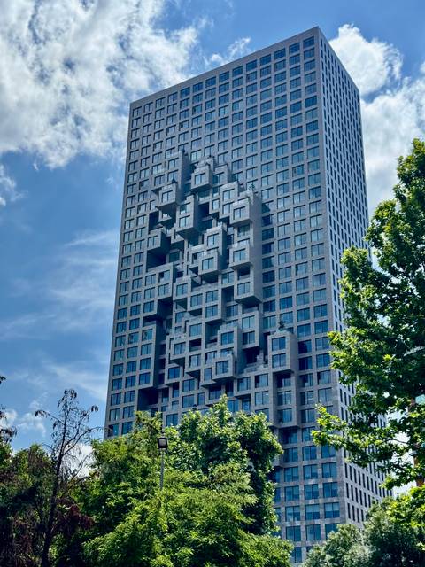 A modern high-rise with an irregular pixelated façade set against a blue summer sky.