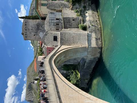 The iconic stone arch of Stari Most bridge spans turquoise waters in Mostar with tourists watching from above.