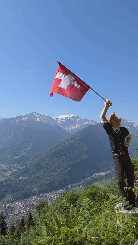 Mountain backdrop with a wooden statue waving the Swiss flag in foreground