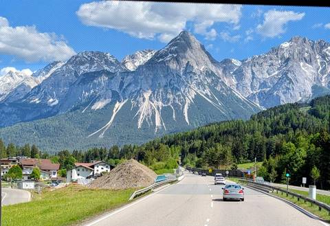 Cars driving toward dramatic Austrian Alps on a sunny day