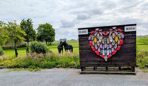 Outdoor display of colorful wooden clogs arranged in a heart shape on a farm fence
