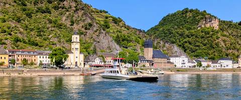 Ferry crossing a picturesque Rhine riverside village under steep green cliffs