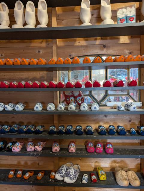 Rows of miniature ceramic clogs in vibrant colors displayed on wooden shelves