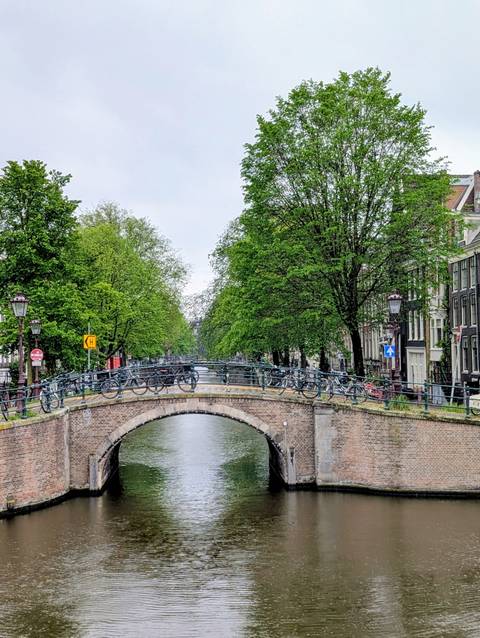 Classic brick bridge lined with parked bicycles over Amsterdam canal on cloudy day