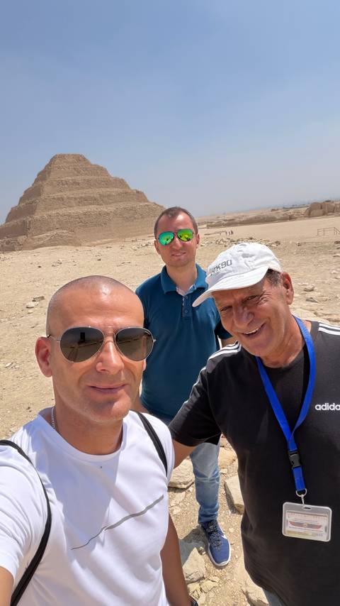 Three men taking a selfie in front of an ancient step pyramid in the desert