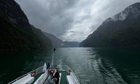 Passenger boat cruising between steep misty mountains on Norway’s Sognefjord.