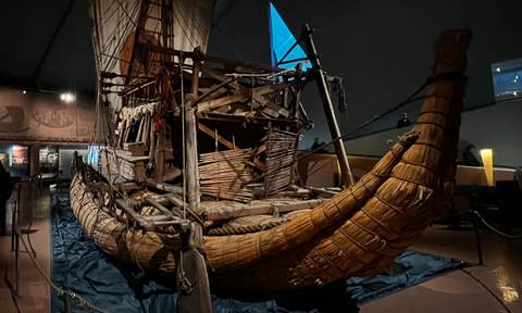 Historic reed raft exhibit inside Oslo's Kon-Tiki Museum under dramatic lighting.