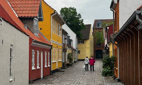 Two women stroll a quiet cobblestone lane lined with pastel half-timbered houses in Odense.