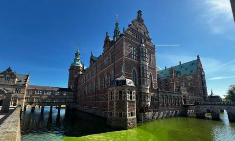 Grand Renaissance-style Frederiksborg Castle surrounded by a moat under a vivid blue sky.