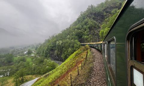 Green train winding through misty mountains on Norway’s famous Flåm Railway.