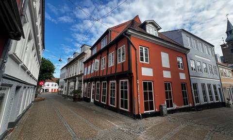 Quiet Danish street with red and white half-timbered house under a partly cloudy sky.