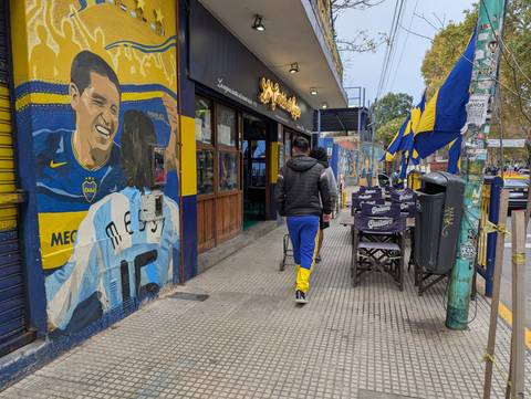 Pedestrian passes a restaurant decorated with a vivid Boca Juniors soccer mural and blue-and-yellow flags in Buenos Aires.