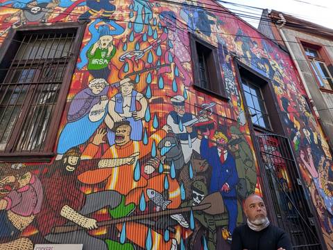 Tall urban mural bursting with colourful caricatures covers the side of a building on a narrow city street.