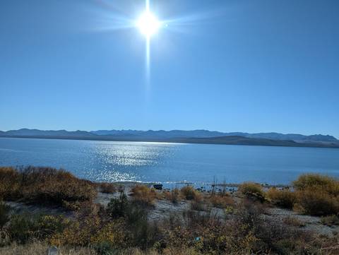 Sunlight sparkles on the surface of a vast blue lake with distant mountain ridges under a cloudless sky.