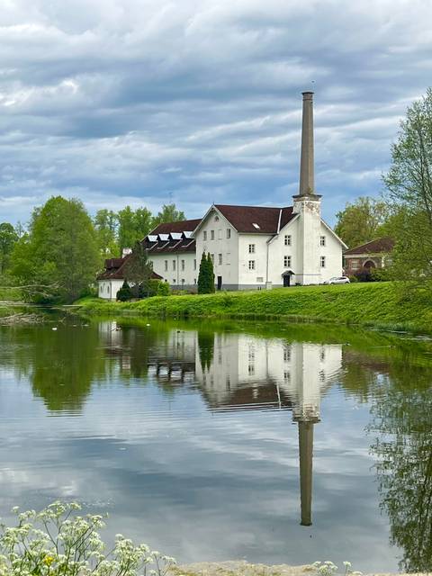 White mill-like building reflected in a tranquil pond surrounded by lush greenery.