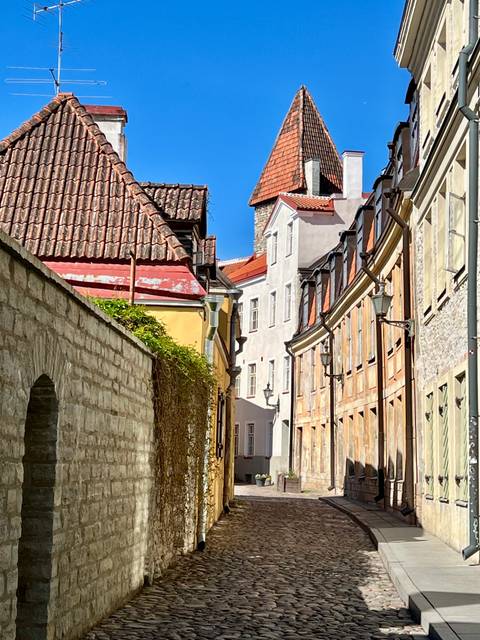 Narrow cobblestone street lined with colourful medieval houses in Tallinn Old Town under clear sky.