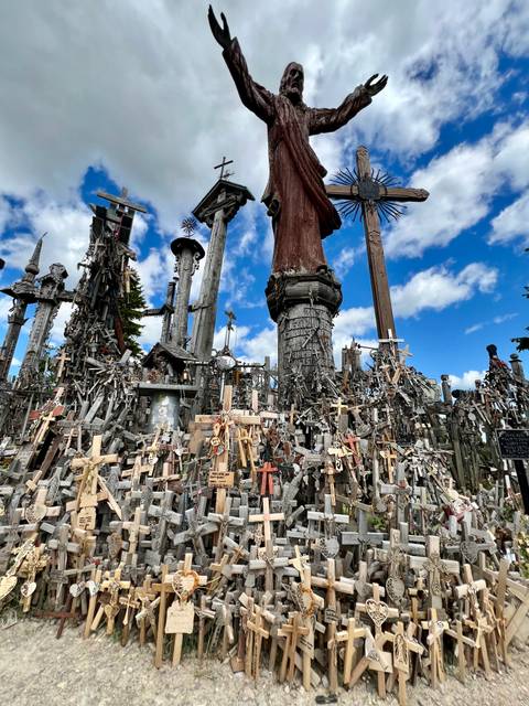 Dense field of thousands of wooden crosses and statues beneath a bright blue sky at the Hill of Crosses.