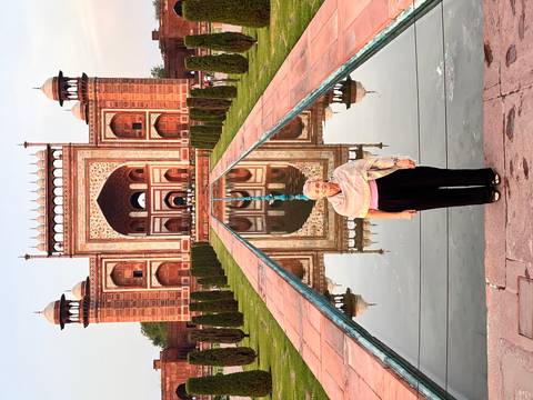 Visitor in front of the grand Mughal gateway reflected in a long pool at the Taj Mahal complex.