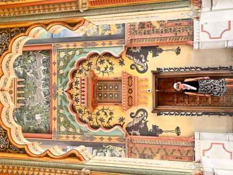 Woman stands before a vividly painted doorway with peacock and floral motifs at Jaipur City Palace.