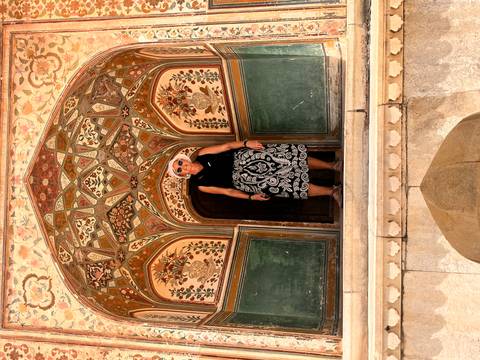 Traveler framed in an ornate archway with detailed frescoes and green painted panels at Amber Fort.