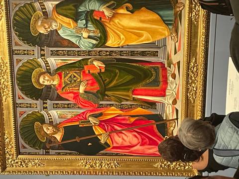 Visitors view a richly colored Renaissance painting showcased in an ornate gold frame.