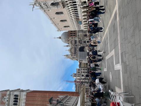 Crowds fill St. Mark’s Square with the basilica and Doge’s Palace under a bright, partly cloudy sky.
