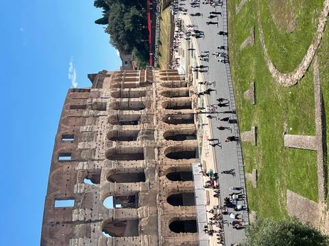 The Colosseum’s ancient arches tower over visitors walking the sunny grounds of Rome’s iconic arena.