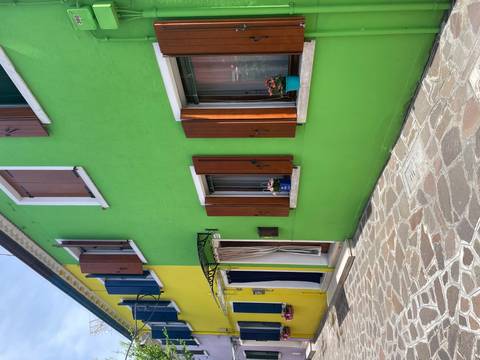 Brightly painted green and yellow houses with wooden shutters line a cobbled lane on Burano island.