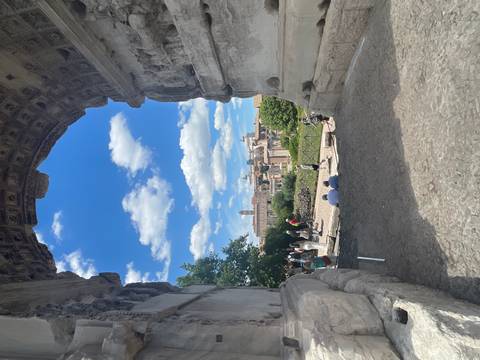 View through a monumental stone arch frames the Roman Forum and distant ruins under blue sky.