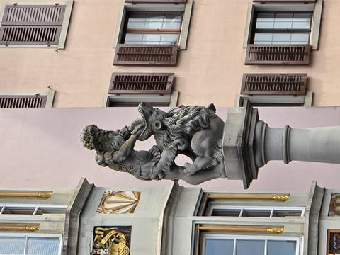 Stone fountain statue of a heroic figure wrestling a lion against pastel building façades