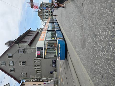 Blue and white Zurich tram number 15 travelling along cobblestone street beside grey civic building