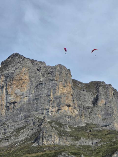 Two colourful paragliders soaring high above a sheer rock cliff in the Swiss Alps