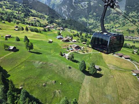 Modern gondola cabin gliding above lush Swiss meadows and scattered chalets