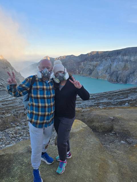 Travellers wearing respirators posing on crater rim with turquoise acid lake in background