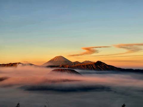 Sea of clouds illuminated by dawn light surrounding layered volcanic peaks of Bromo Tengger massif