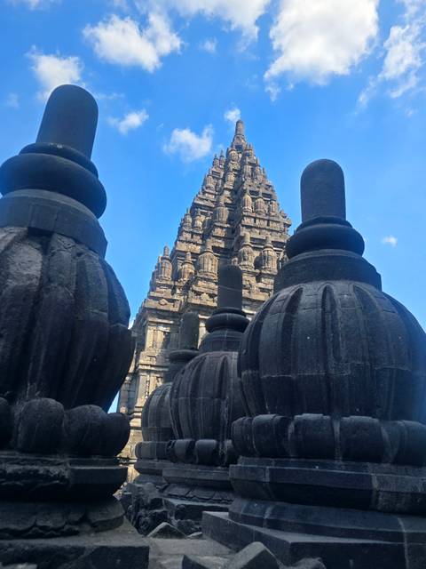 Stone stupas and ornate tower of a historic Javanese temple complex against blue sky