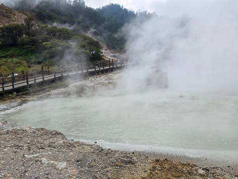 Steaming sulphur hot spring pool with wooden boardwalk in misty volcanic landscape