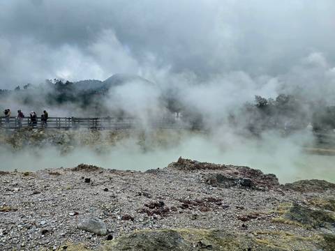 Visitors observe steaming turquoise pools across a rocky volcanic field