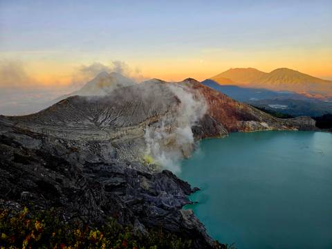Sulphur steam rises from bright turquoise crater lake amid rugged volcanic peaks at dawn