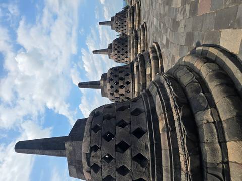 Row of bell-shaped stupas lining the upper terraces of Borobudur beneath scattered clouds