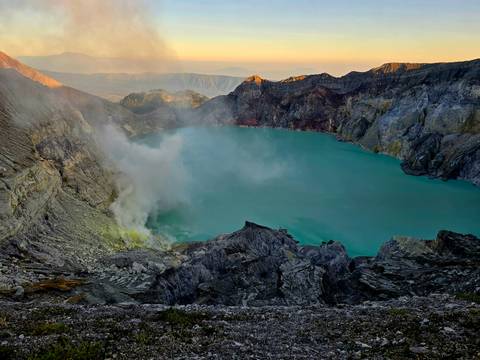 Wide view of turquoise Ijen crater lake with steam plume curling into sunrise sky