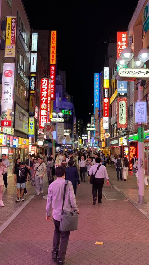Bustling neon-lit Tokyo street packed with evening crowds and colorful shop signs