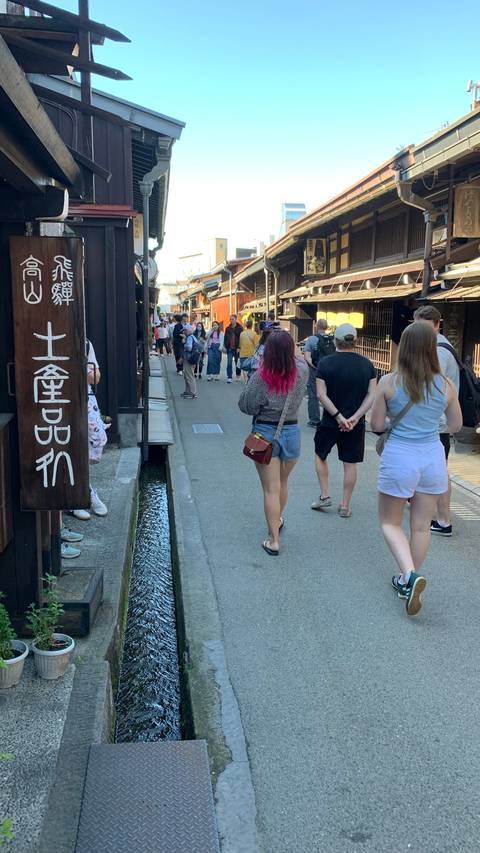 Visitors wander a traditional wooden street lined with shops and canals in Takayama