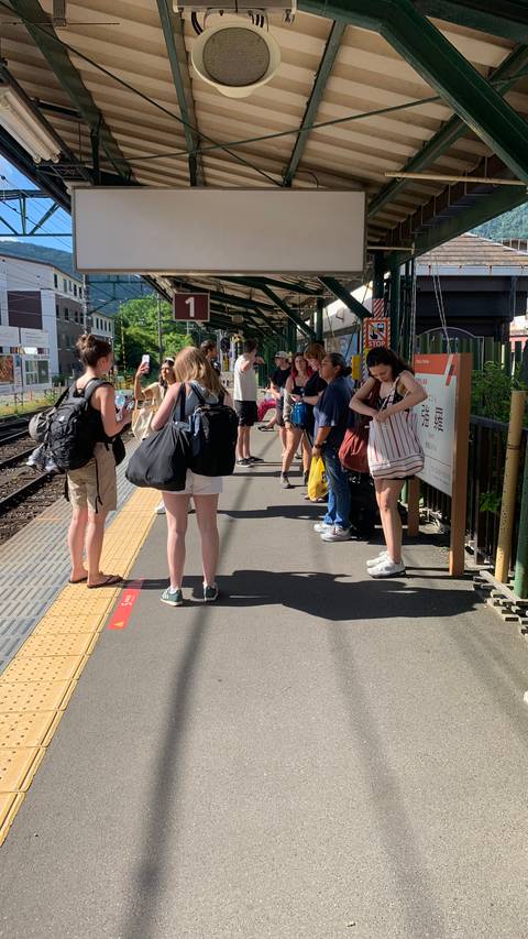 Group of travelers with backpacks waiting on a sunny outdoor train platform