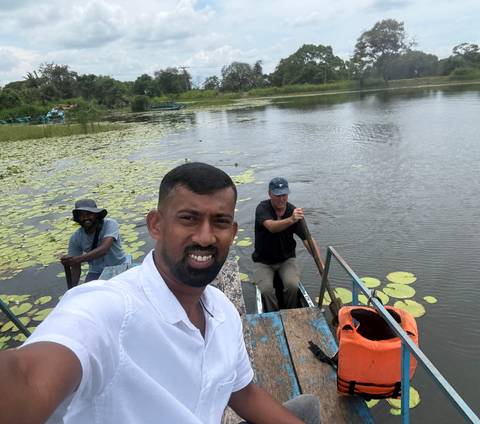 Guide taking selfie with tourist while paddling a small boat on a lily-covered lake.