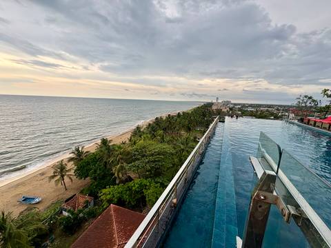 Rooftop infinity pool overlooking long sandy coastline and cityscape at dusk.