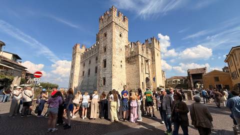 Crowd of tourists gathered outside a medieval stone castle tower on a sunny day.
